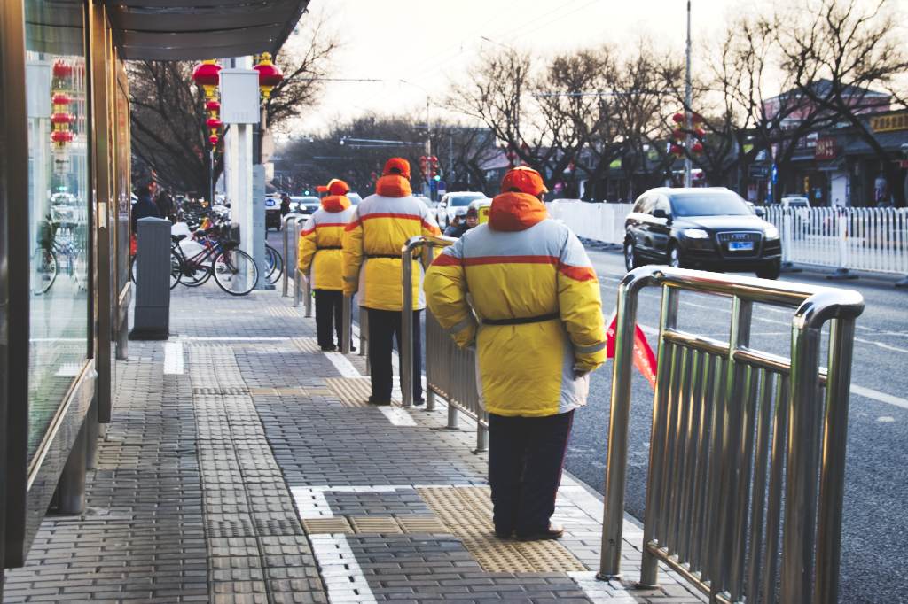 Bushaltestelle mit Helfern in gelben Jacken in der Andingmen Inner Street in Peking