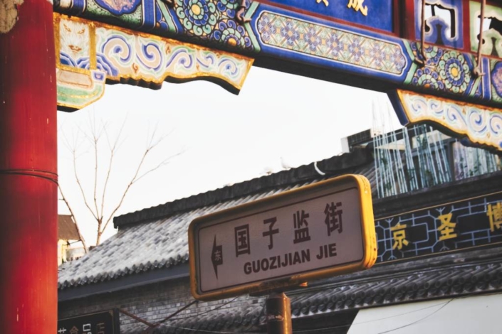 Straßenschild: Guozijian Jie in Peking, eingerahmt vom Torbogen