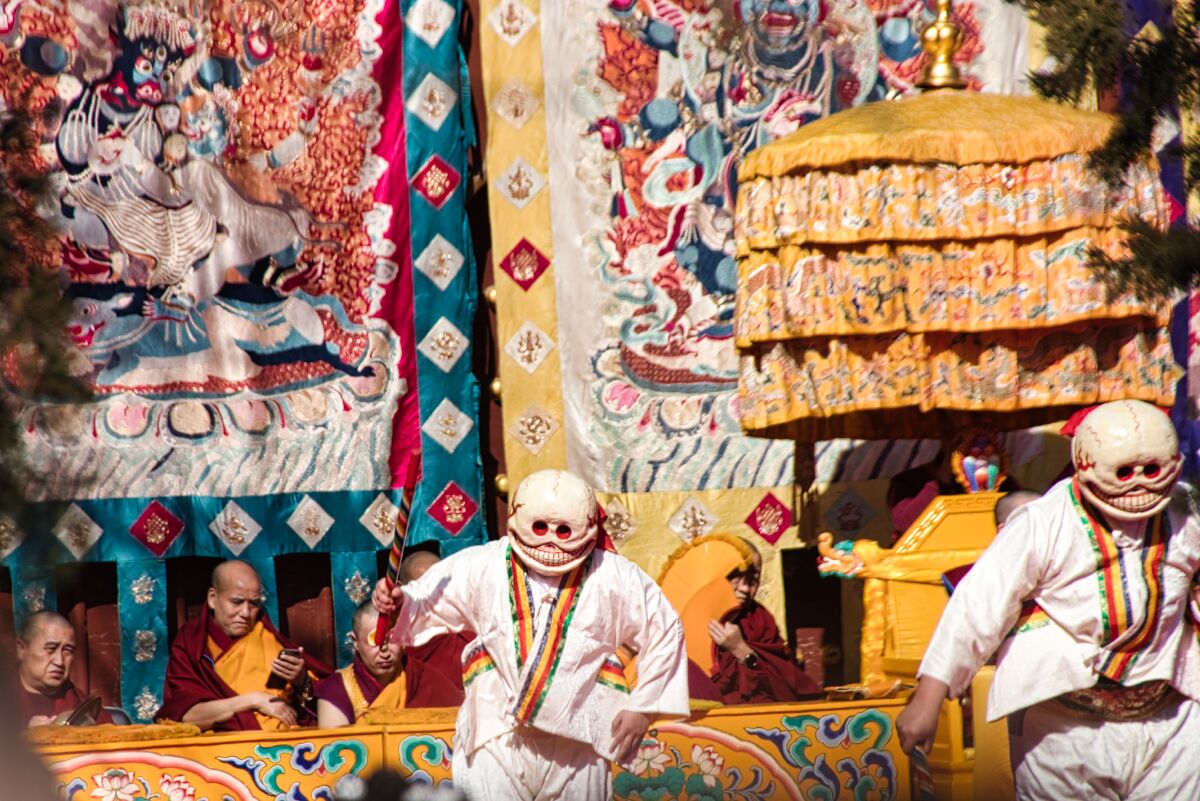 Losar im Lamatempel: zwei verkleidete Mönche tanzen den Devil's Dance, im Hintergrund bunte Thangkas und weitere Mönche.